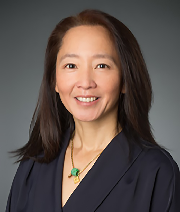 Photo of TAG board member Julian Chung. Asian woman with dark hair and eyes, smiling, wearing a black v-necked top and a gold necklace