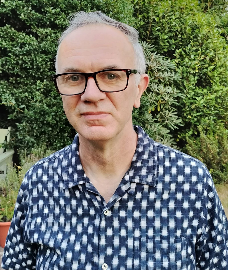 White male with glasses and grey hair, wearing a blue and white checked shirt with a collar and buttons