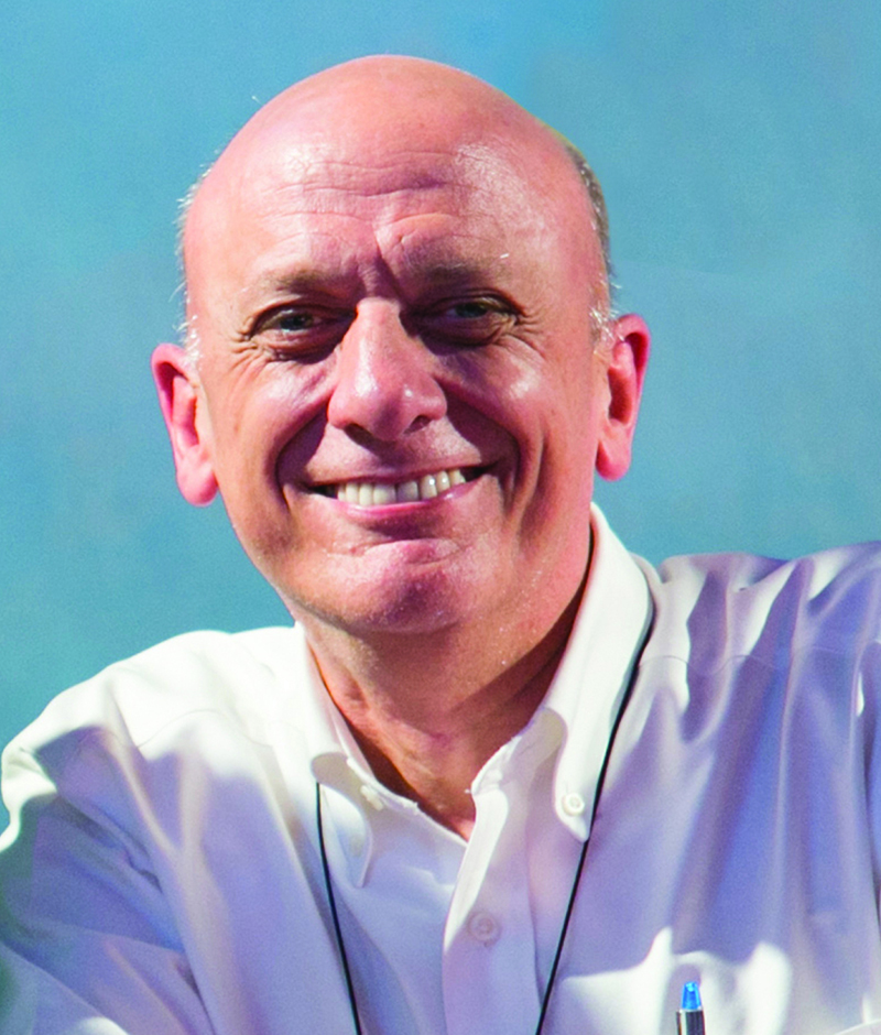 white man, bald, smiling broadly, wearing a white button down shirt.